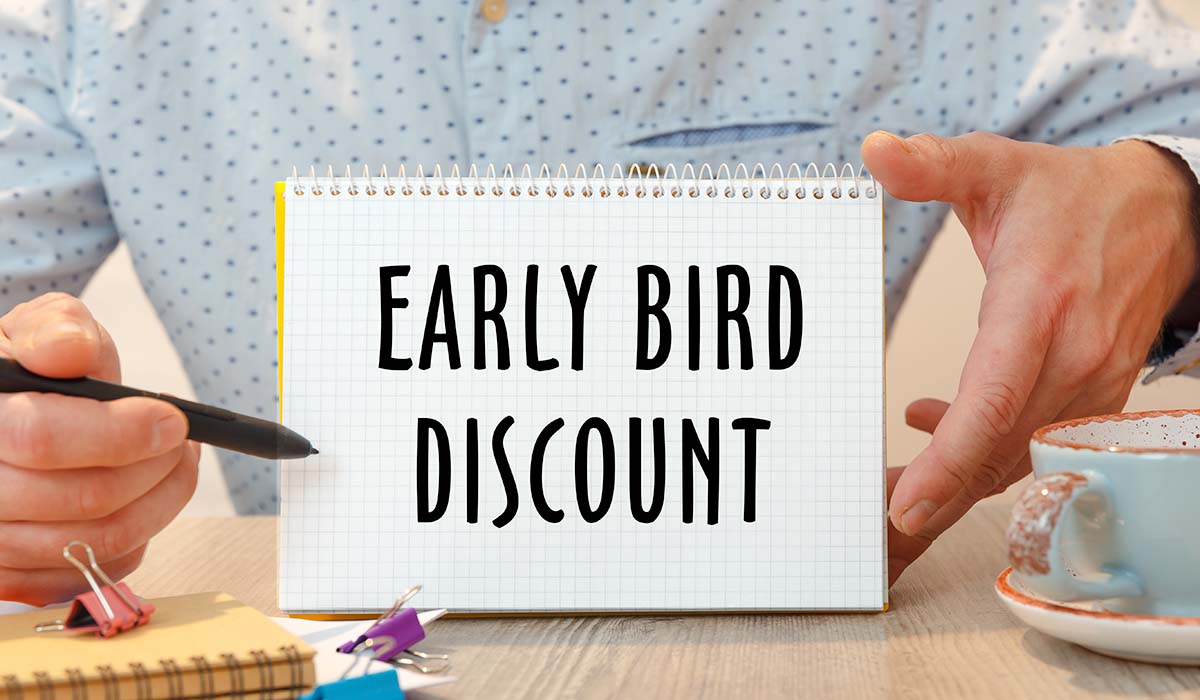 Man wearing dotted shirt holding up an Early Bird Discount message on a notebook
