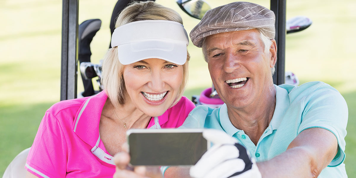 Golfers wearing blue and pink smiling in a golf cart while using a charity golf tournament software application on their mobile phone.