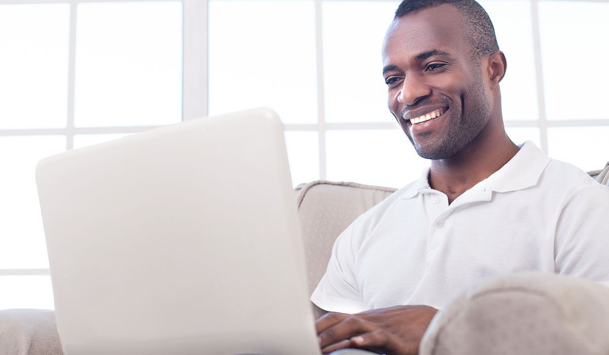 African american man sitting on couch with laptop