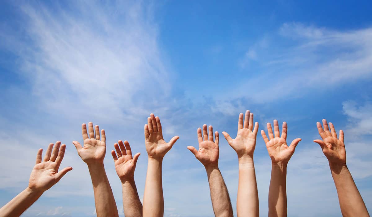 Eight raised hands towards a blue sky