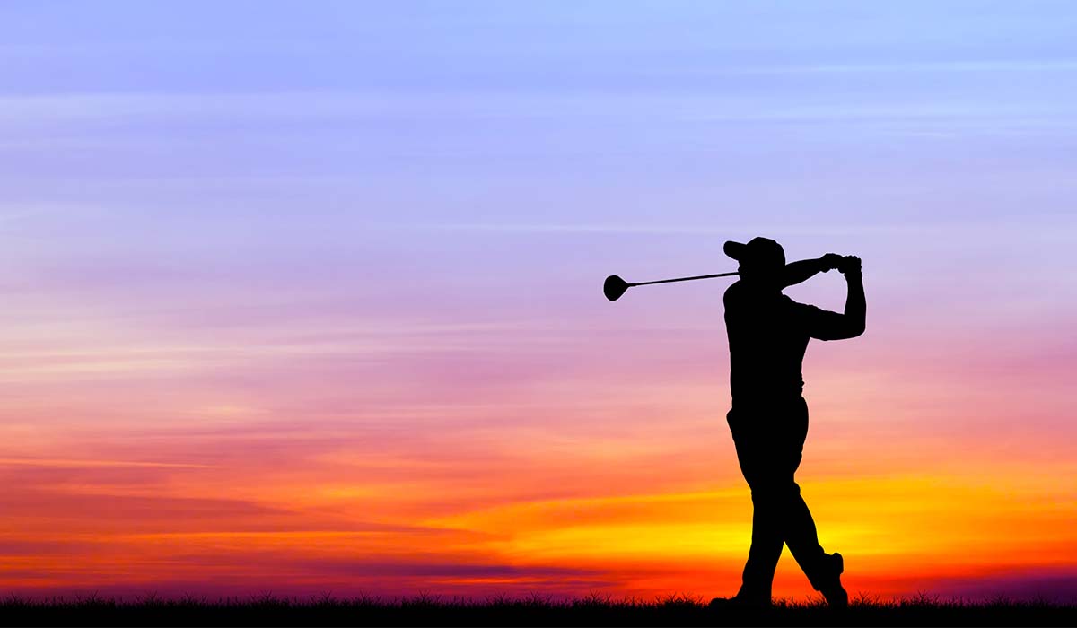 Silhouette of golfer swinging club with sunrise sky behind him